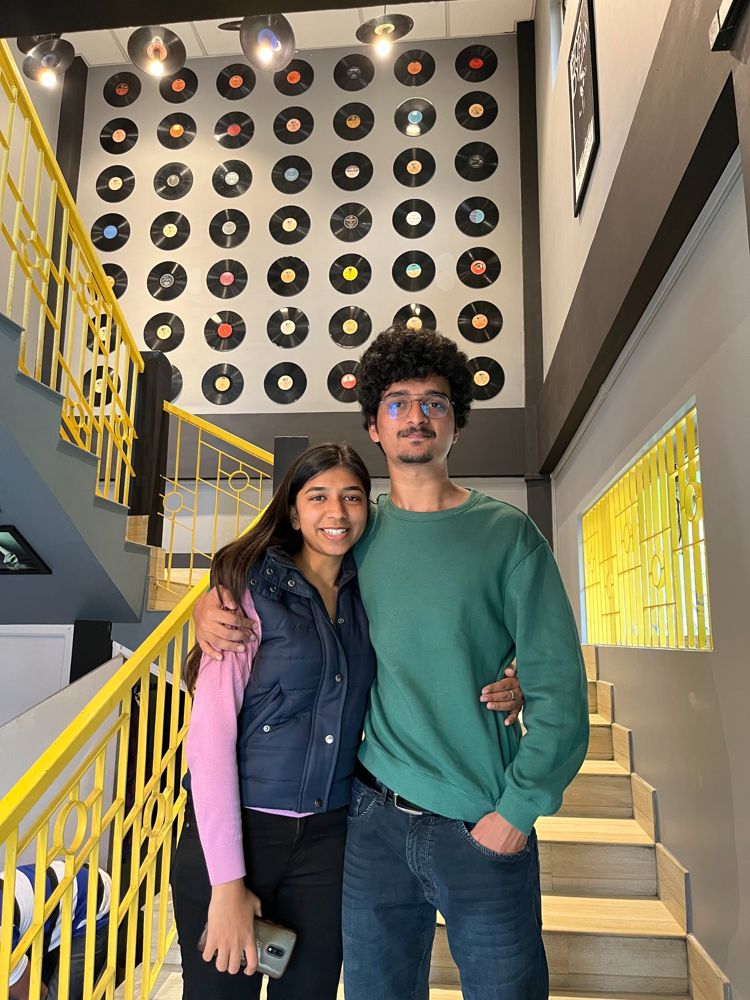 Urvish and Unnati at a café with a wall of vinyl records